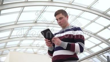 一个年轻人拿着一块石碑站着。 一个人用平板电脑抵住玻璃屋顶。 一个忙碌的人正在发短信